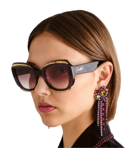 Close-up of a person wearing large sunglasses and colorful earrings on a white background
