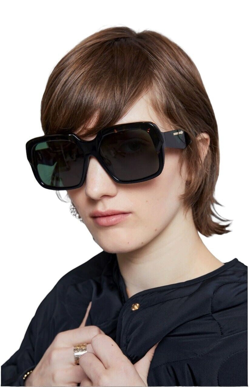 Model wearing Naked Pear Karen Walker Asscher oversized square black bio-acetate sunglasses with green tinted lenses