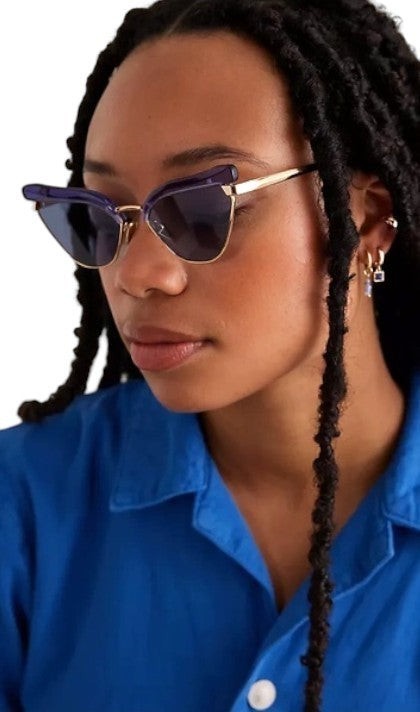 Model wearing Naked Pear Karen Walker Fantasia cat eye sunglasses with blue acetate, gold metal, and indigo lenses.