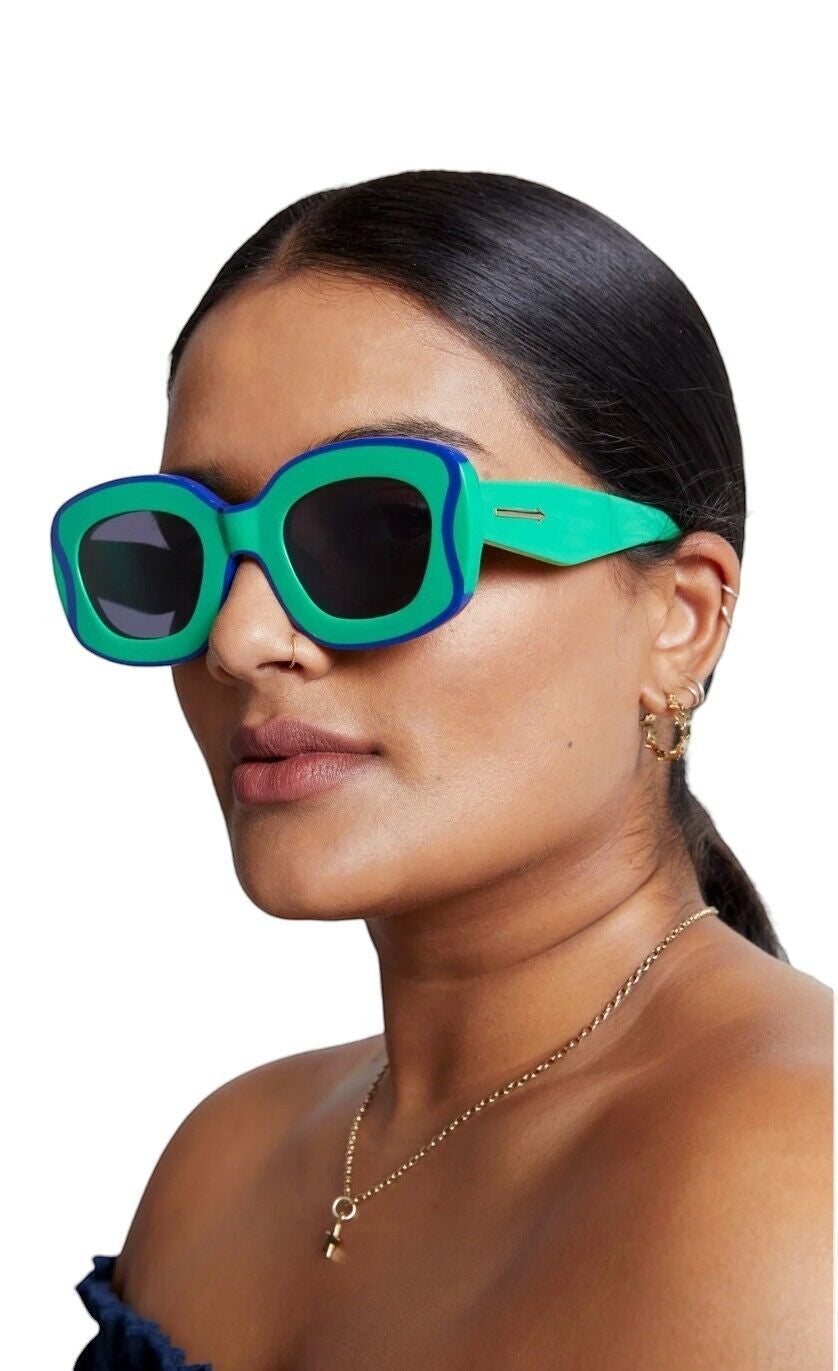 Model wearing Naked Pear Karen Walker Field Trip sunglasses in grasshopper green acetate with blue wavy lamination.