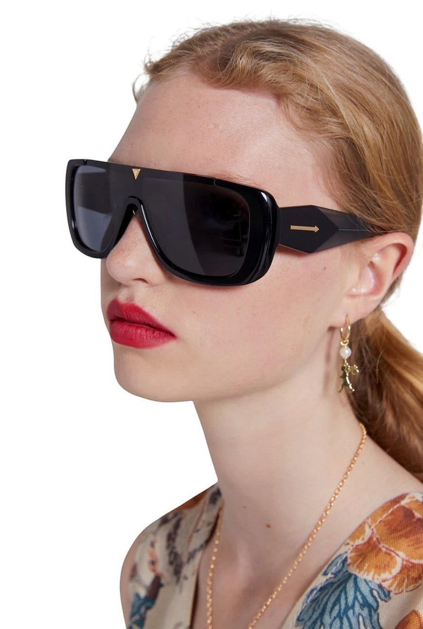 Naked Pear Karen Walker Hexed B black shield sunglasses with gold-tone hardware worn by a model