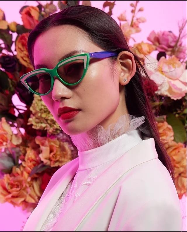Naked Pear model wearing Karen Walker Lash Splash green and purple cat-eye bio-acetate sunglasses with grey lenses.