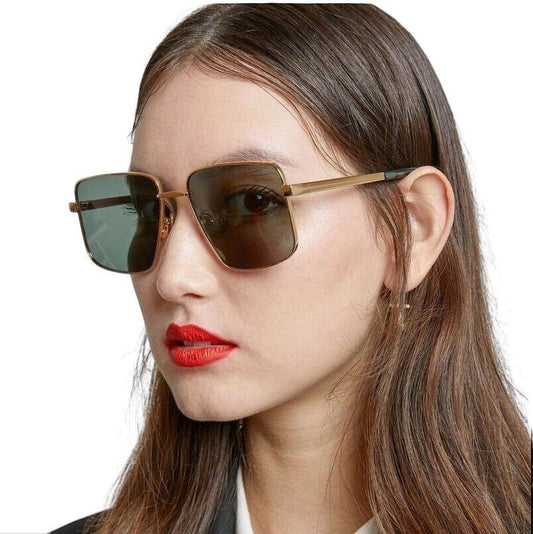 A model wearing Naked Pear Karen Walker Nada oversized square aviator sunglasses with gold frames and green lenses.