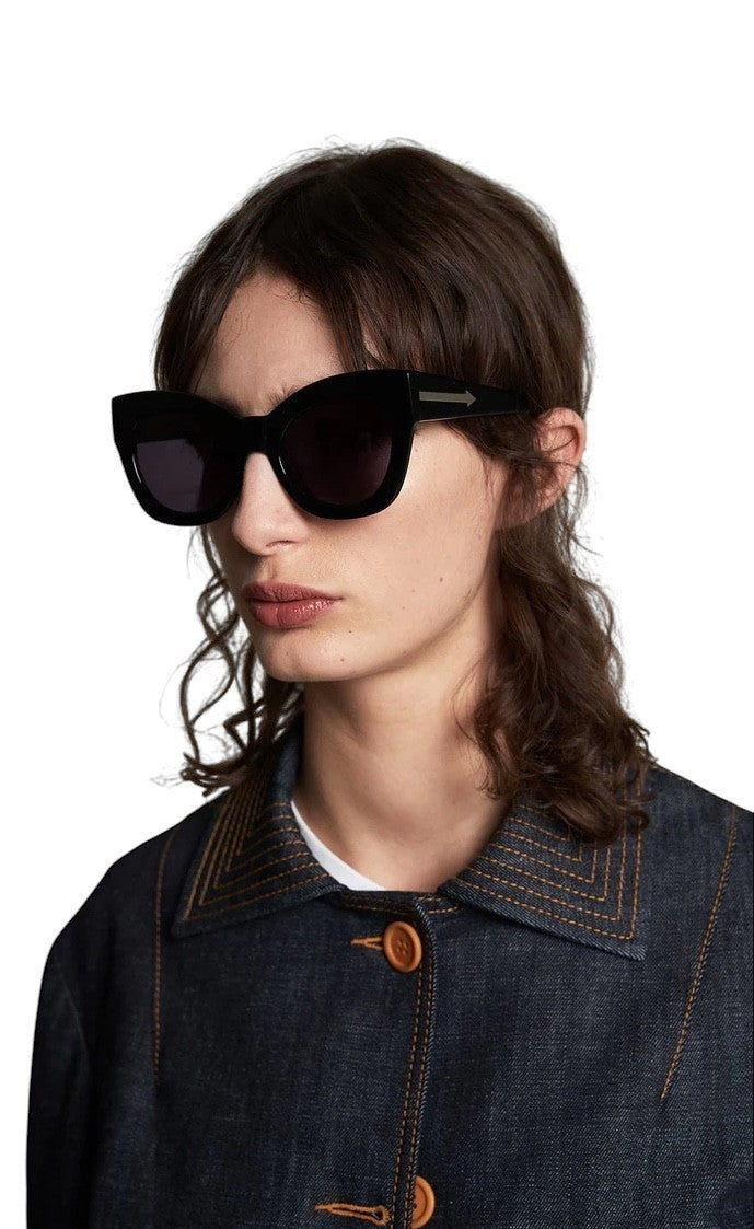 Model wearing Naked Pear Karen Walker Northern Lights cat-eye sunglasses with black acetate frames and grey lenses.