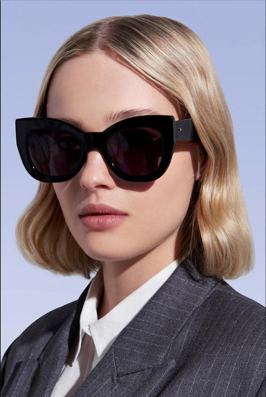 Naked Pear Karen Walker Northern Lights oversized black cat-eye sunglasses with grey lenses worn by a blonde model