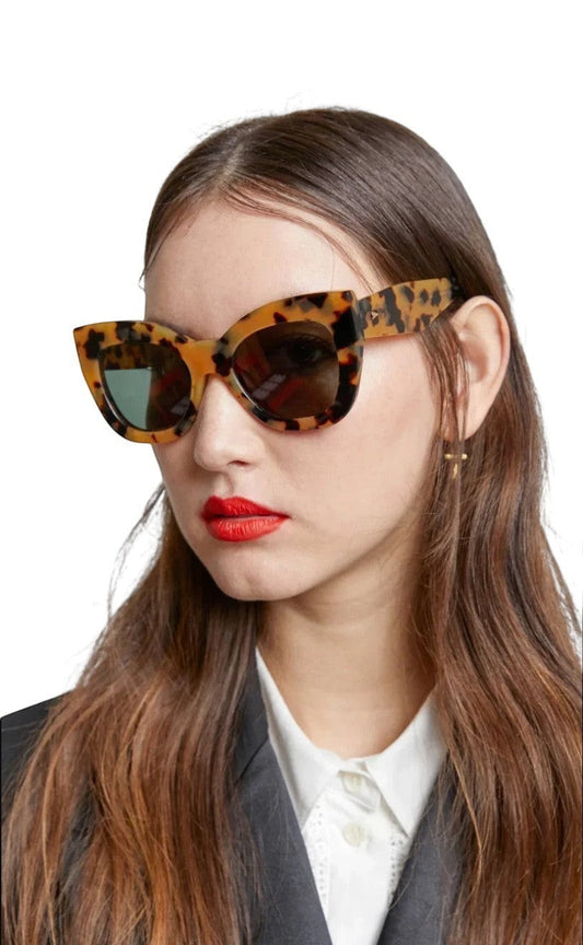 Model wearing Naked Pear Karen Walker Northern Lights oversized cat-eye sunglasses in tortoise shell with green lenses