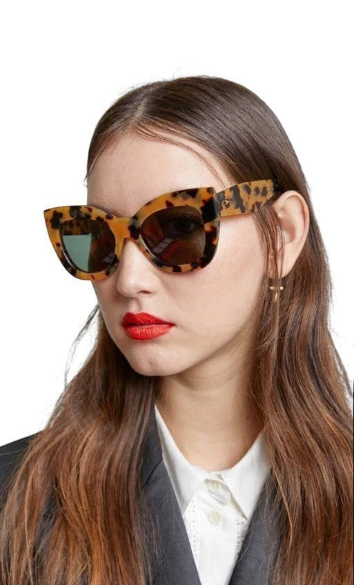 Model wearing Naked Pear Karen Walker Northern Lights oversized cat-eye sunglasses in tortoise shell with green lenses
