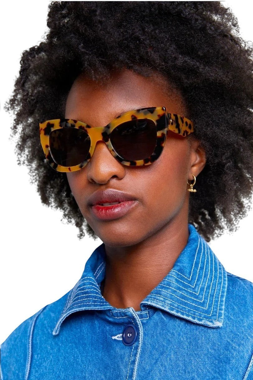 Model wearing Naked Pear Karen Walker Northern Lights oversized cat-eye sunglasses in tortoise shell with green lenses