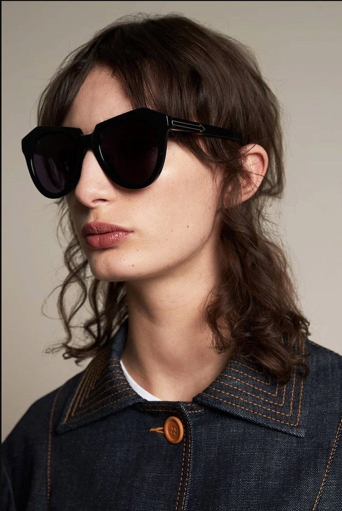 Model wearing Naked Pear Karen Walker Number One black bio-acetate cat-eye sunglasses with grey smoke mono lenses.
