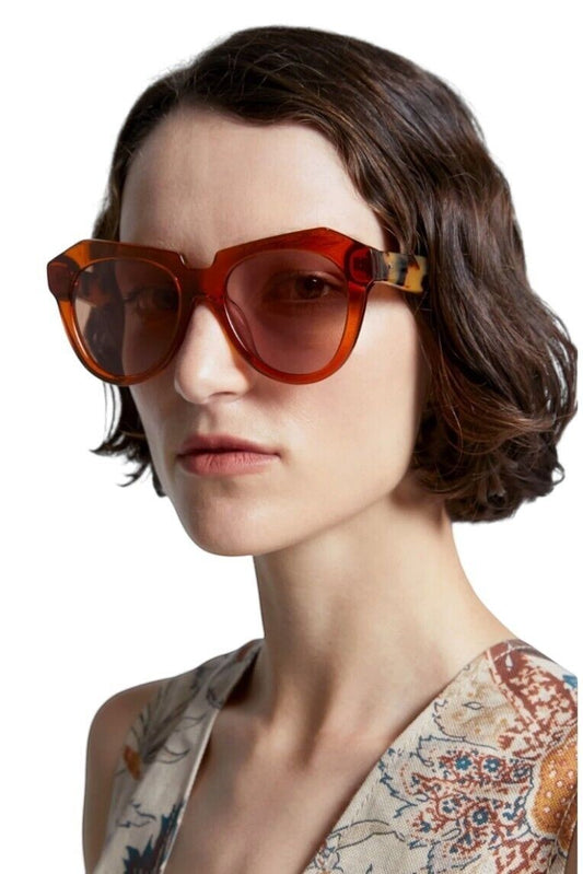 Model wearing Naked Pear Karen Walker Number One oversized cat-eye sunglasses in persimmon and tortoise shell acetate
