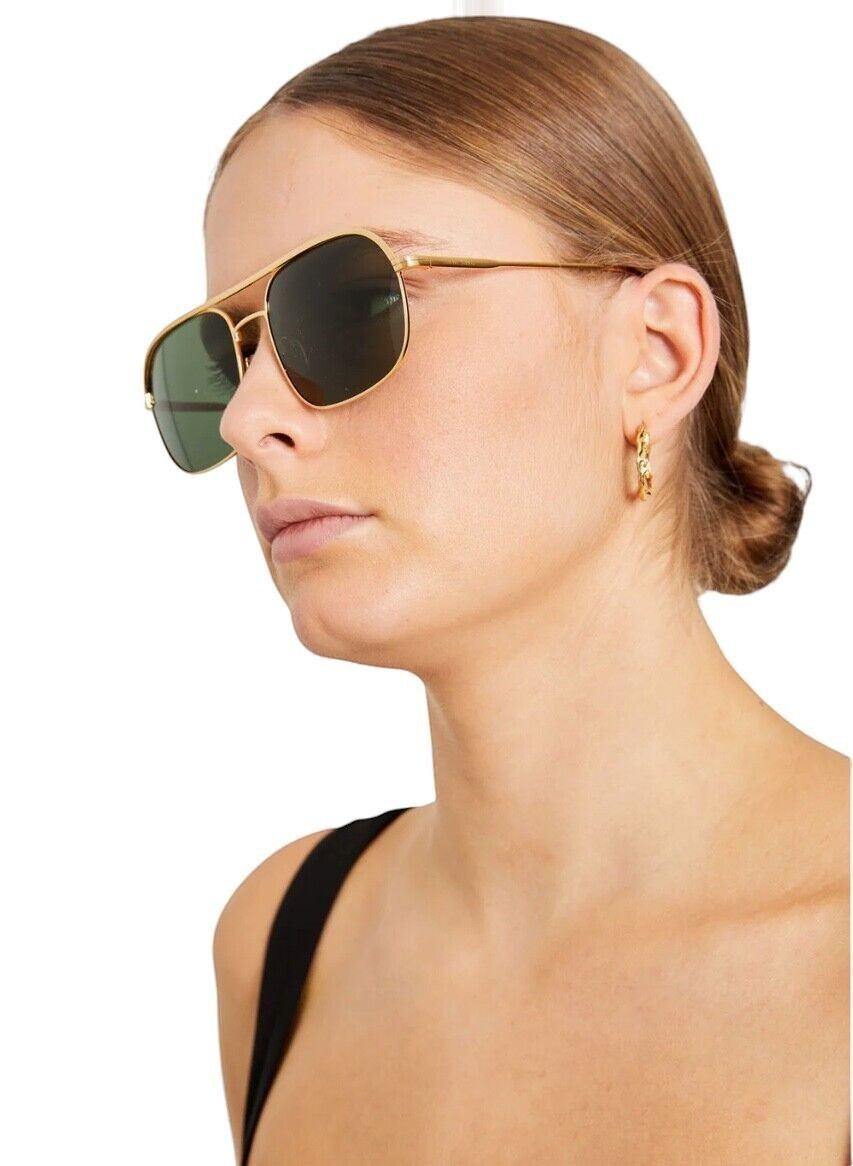 A model wearing Naked Pear Karen Walker Pampel aviator sunglasses with gold frames and grass-green lenses.