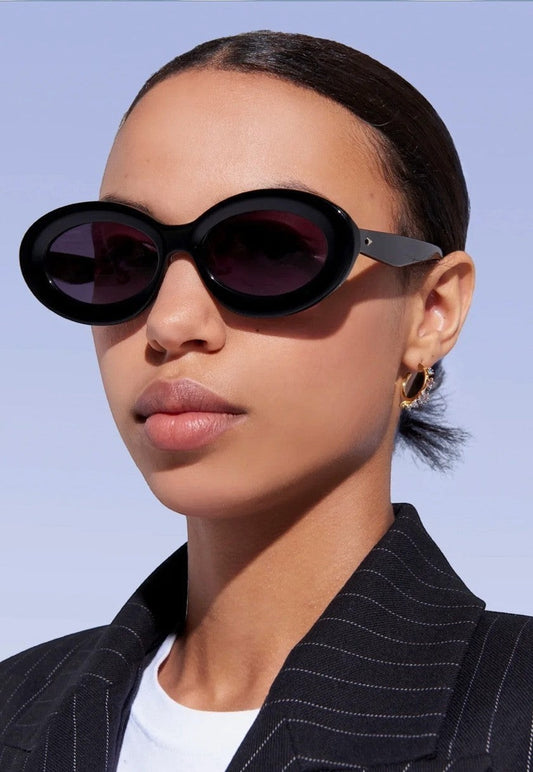 Model wearing Naked Pear Karen Walker Rapture B oval black bio-acetate sunglasses with grey lenses