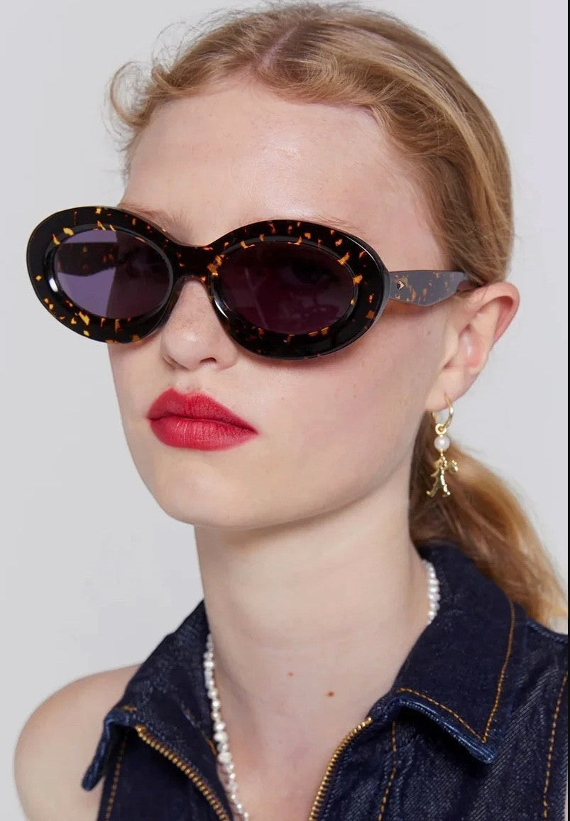 Model wearing Naked Pear Karen Walker Rapture B oval sunglasses in cracked tortoise shell bio-acetate with grey lenses