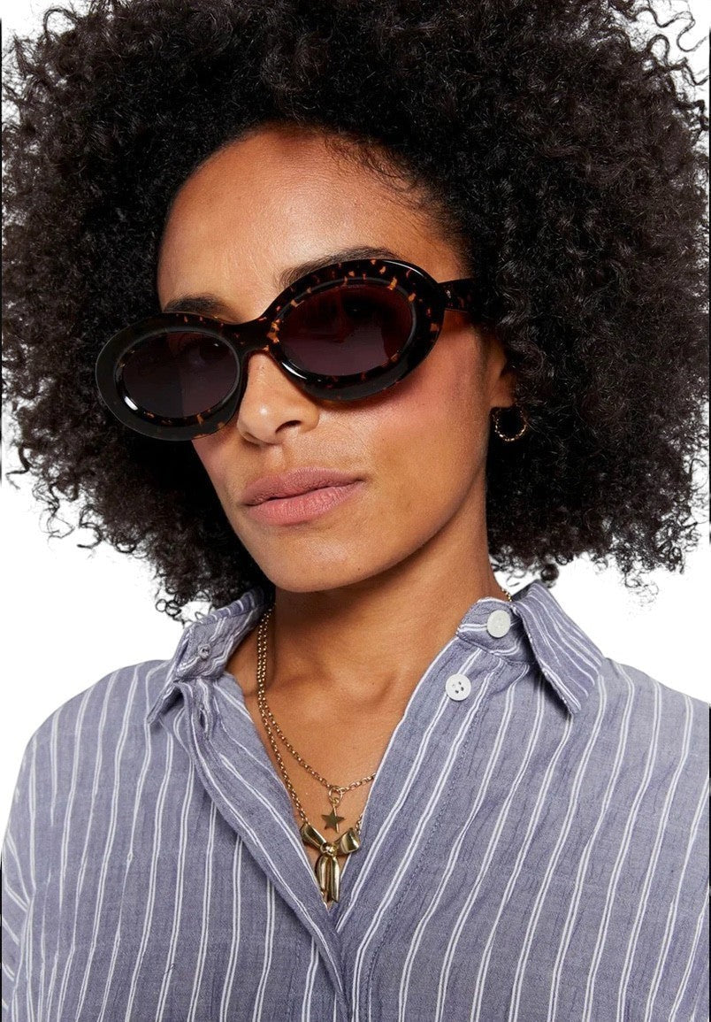 Model wearing Naked Pear Karen Walker Rapture B oval sunglasses in cracked tortoise shell with grey mono lenses.