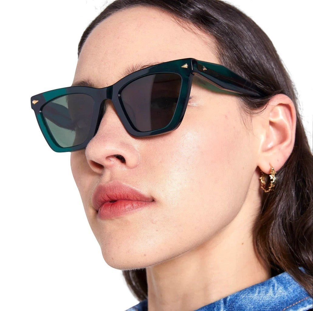 Model wearing Naked Pear Karen Walker Spellbound emerald green cat-eye acetate sunglasses with gold arrow hardware