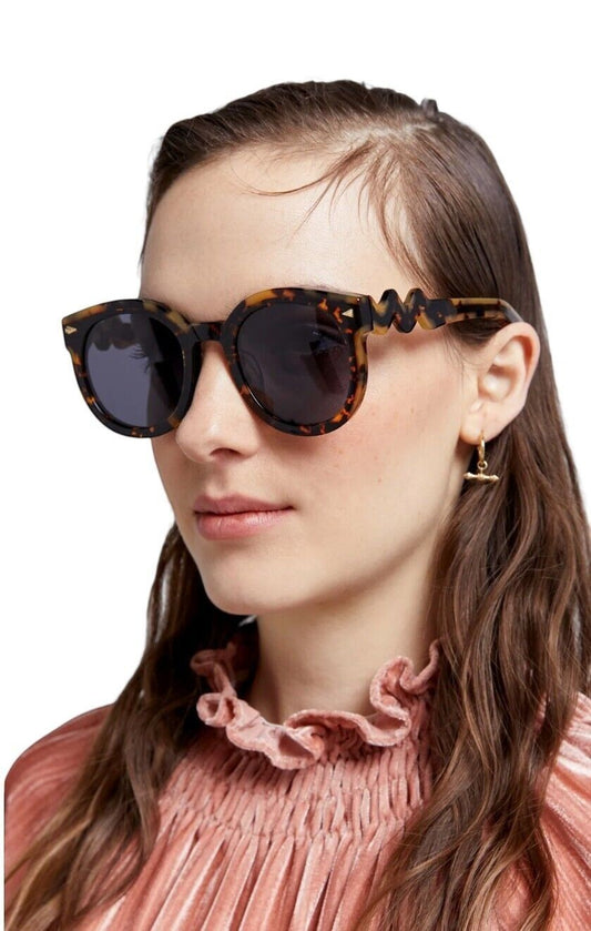 Model wearing Naked Pear Karen Walker Super Wavy Duper round tortoise shell sunglasses with unique wavy arms.