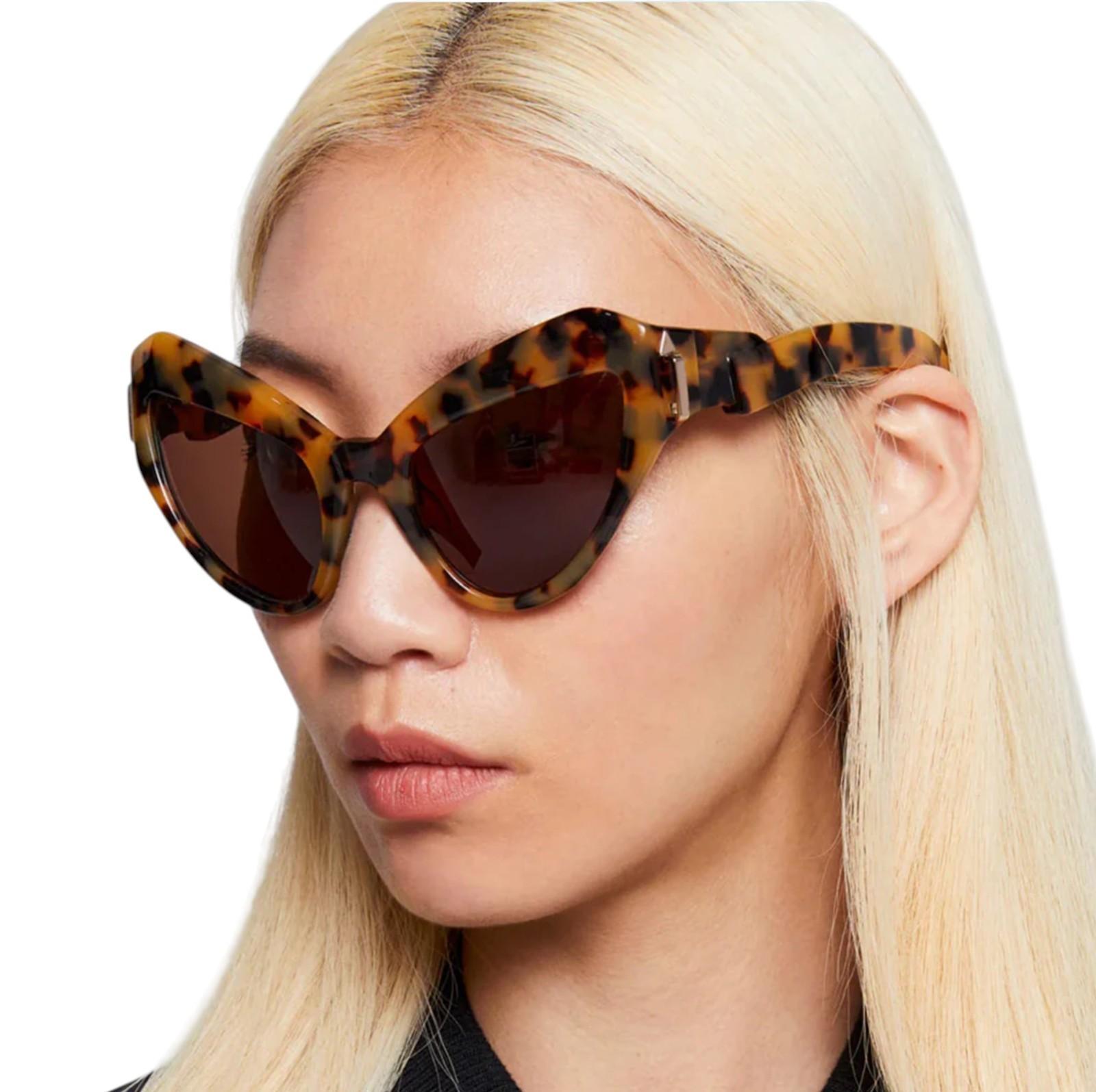 Person wearing tortoiseshell cat-eye sunglasses with a neutral background