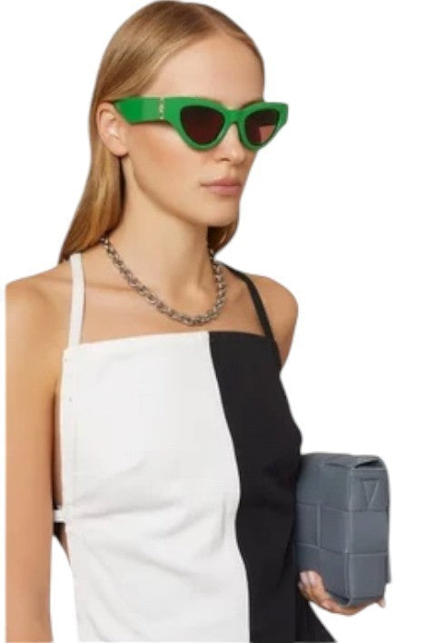 Woman wearing green sunglasses and holding a gray clutch against a white background