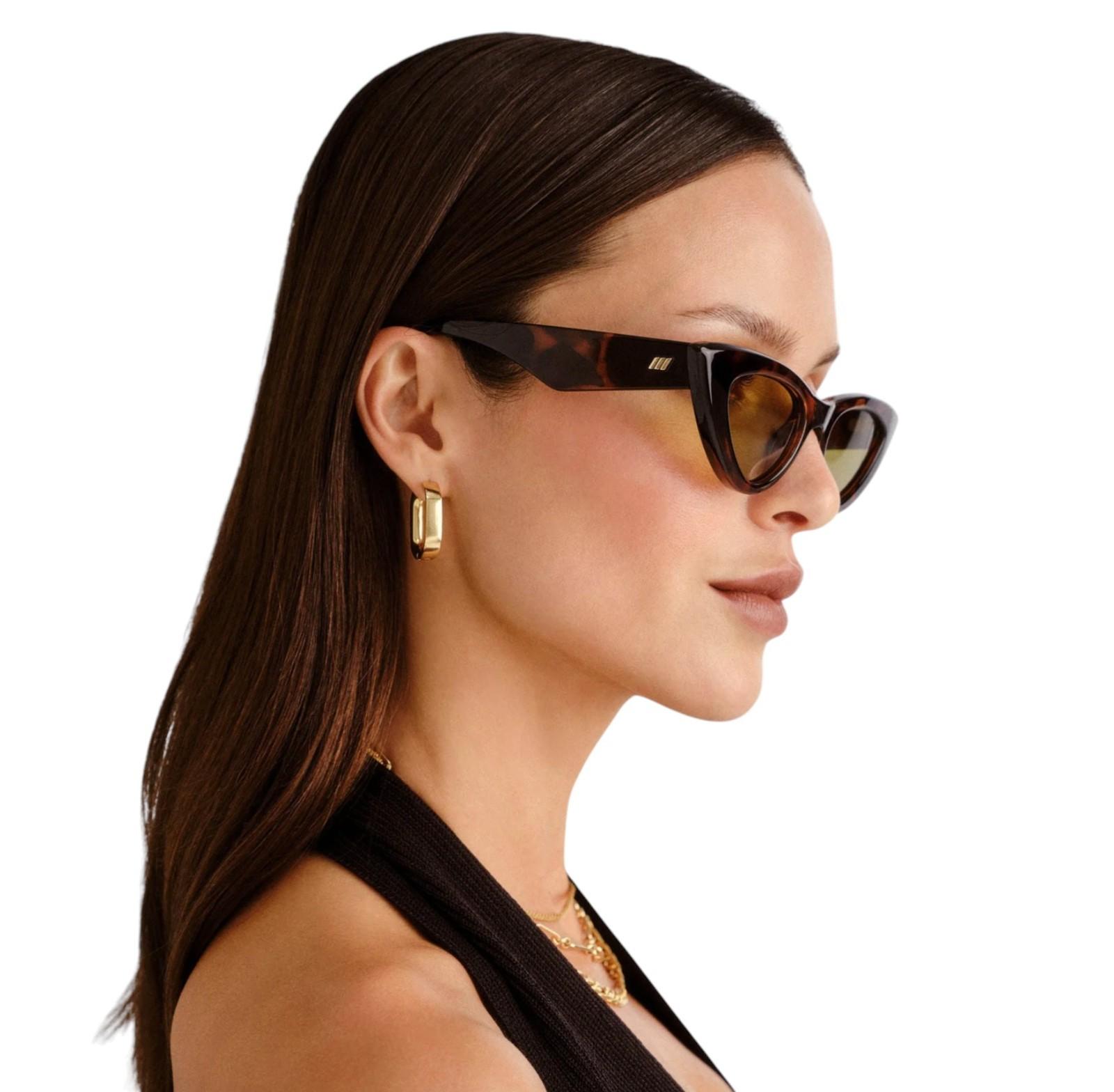 Woman wearing tortoiseshell sunglasses with a plain background