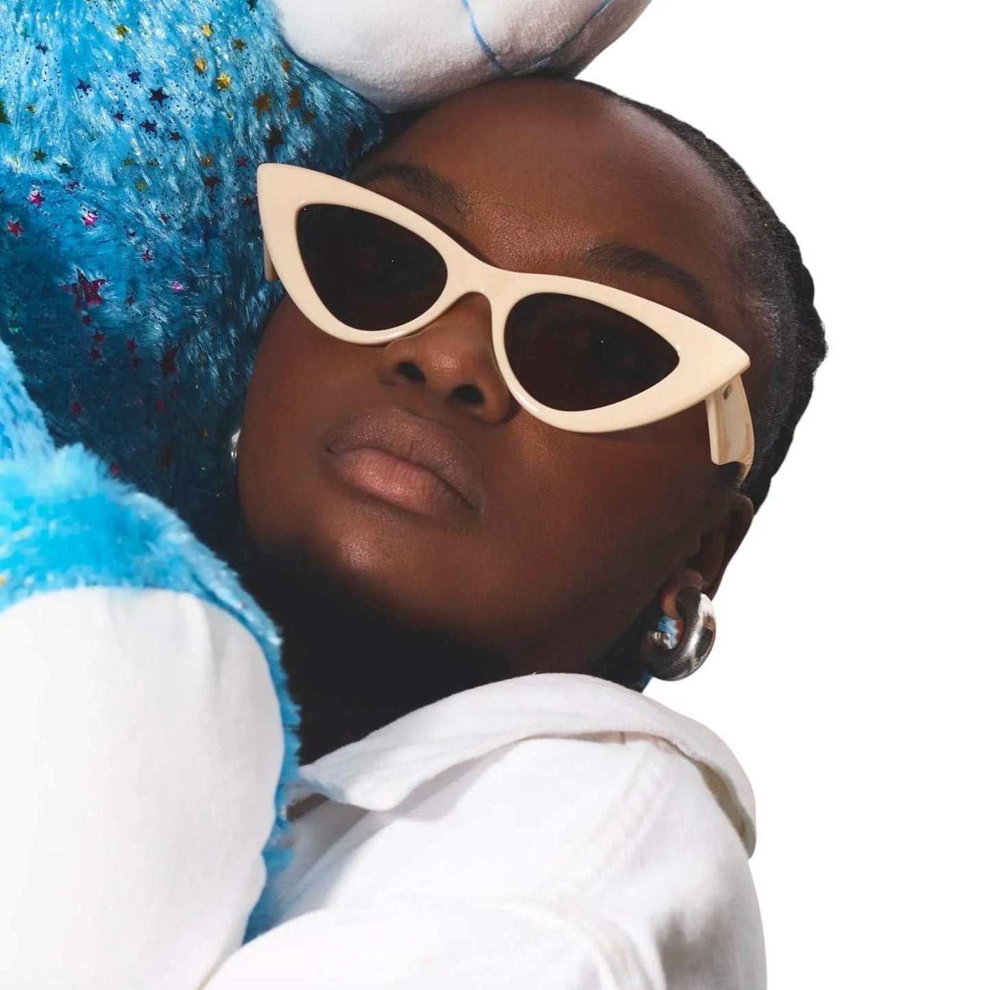 Person wearing cat-eye sunglasses with a blue plush toy on a white background