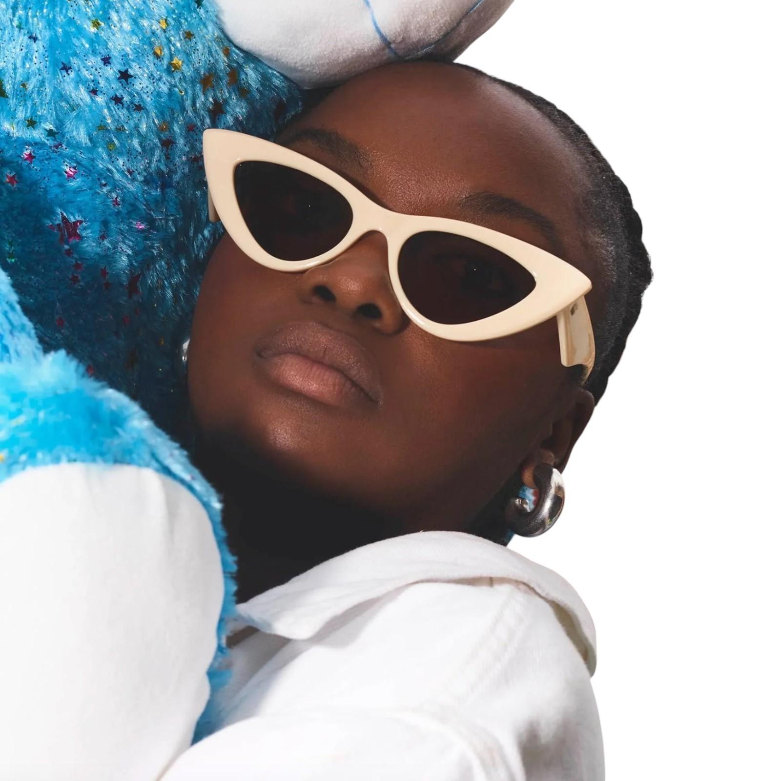 Person wearing cat-eye sunglasses with a blue plush toy on a white background