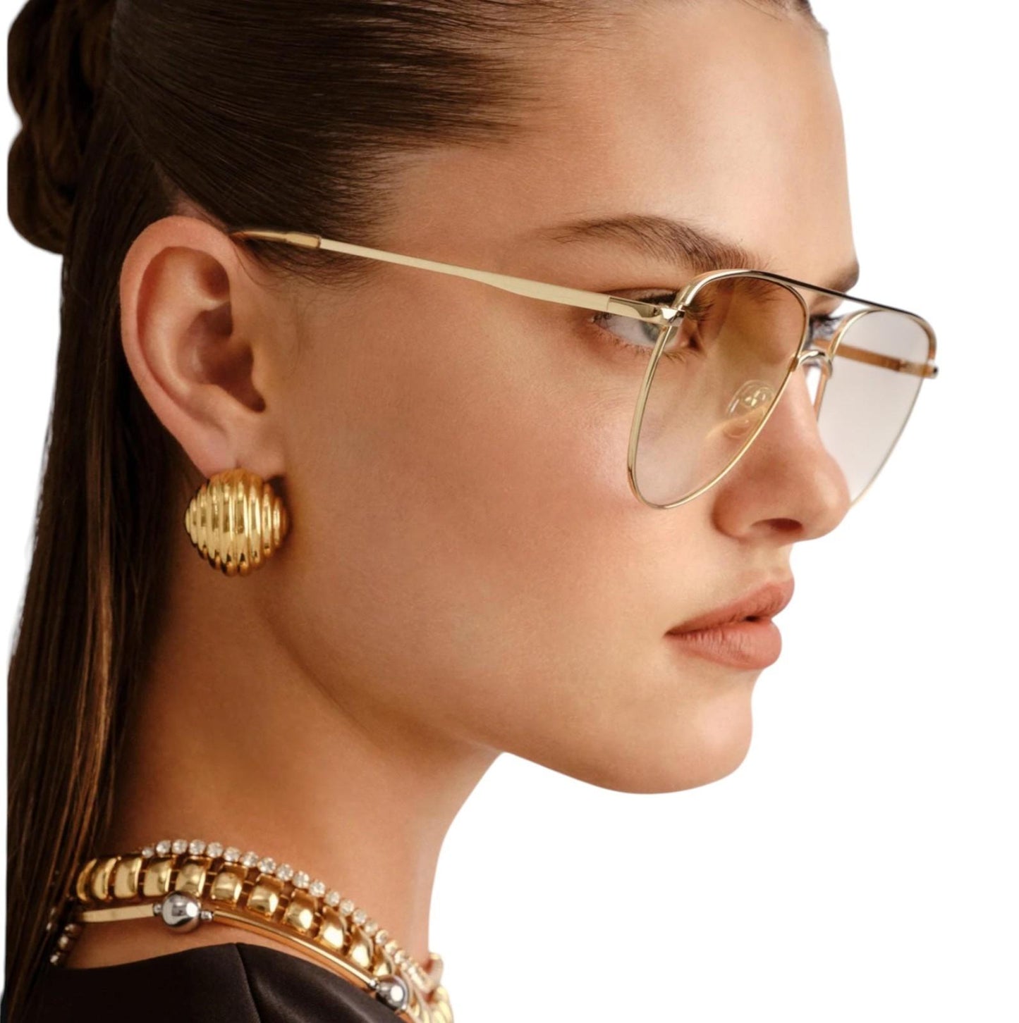 Woman wearing gold sunglasses and earrings with a neutral background