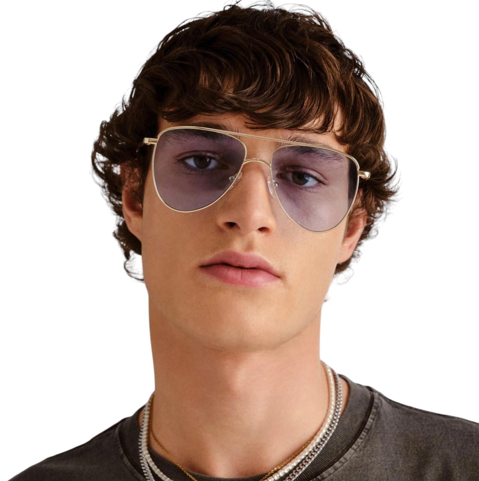 Person wearing gold-framed sunglasses with a plain background