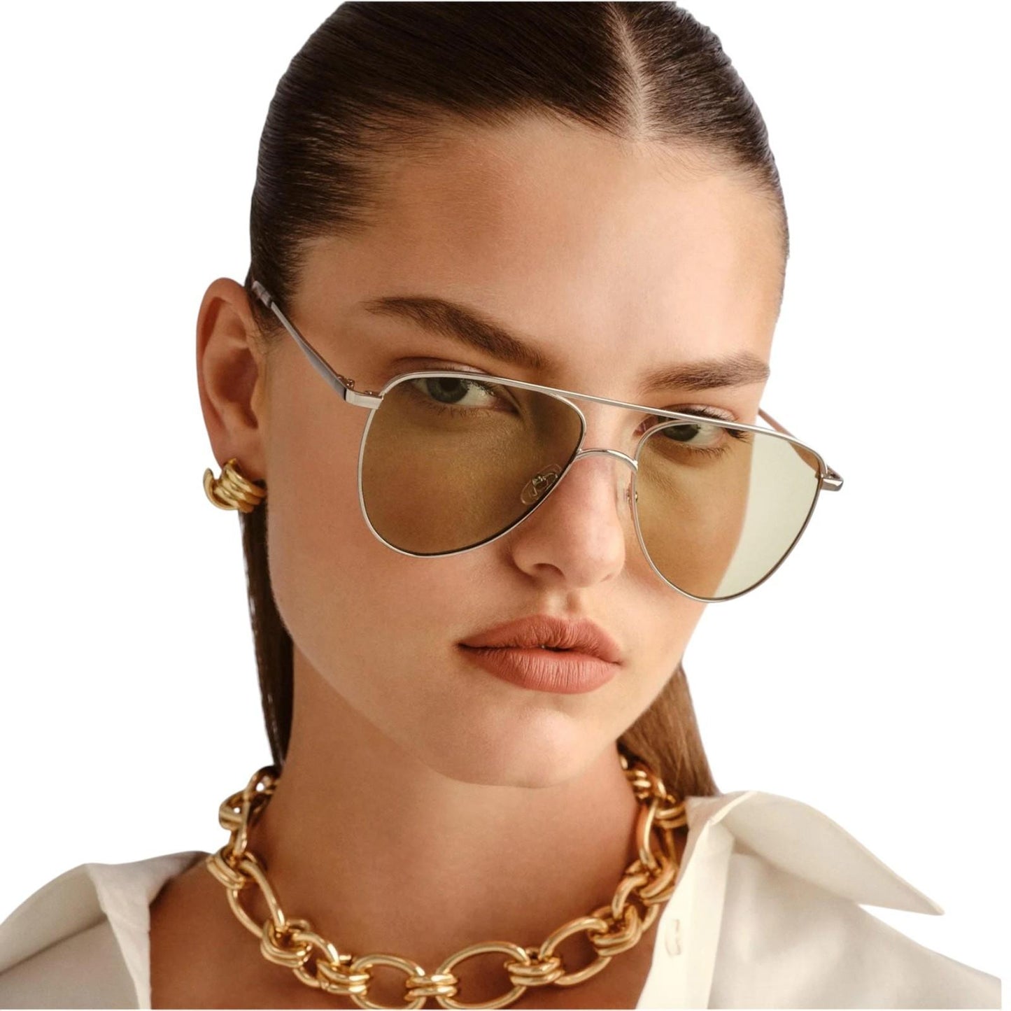 Woman wearing gold sunglasses and a gold chain necklace on a white background