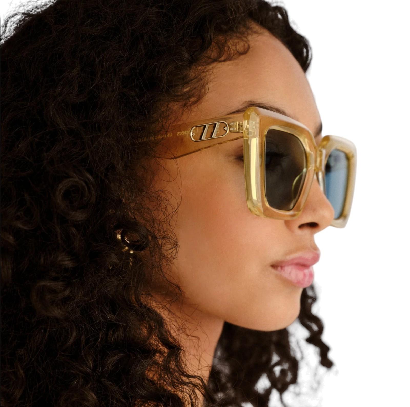 Woman wearing gold sunglasses with a neutral background