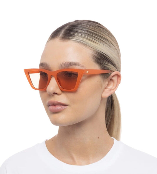 A person wearing orange cat-eye style sunglasses with angular acetate frames.
