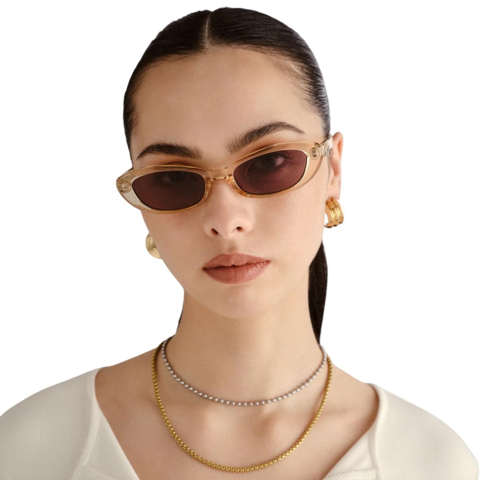 Woman wearing gold sunglasses and jewelry on a white background