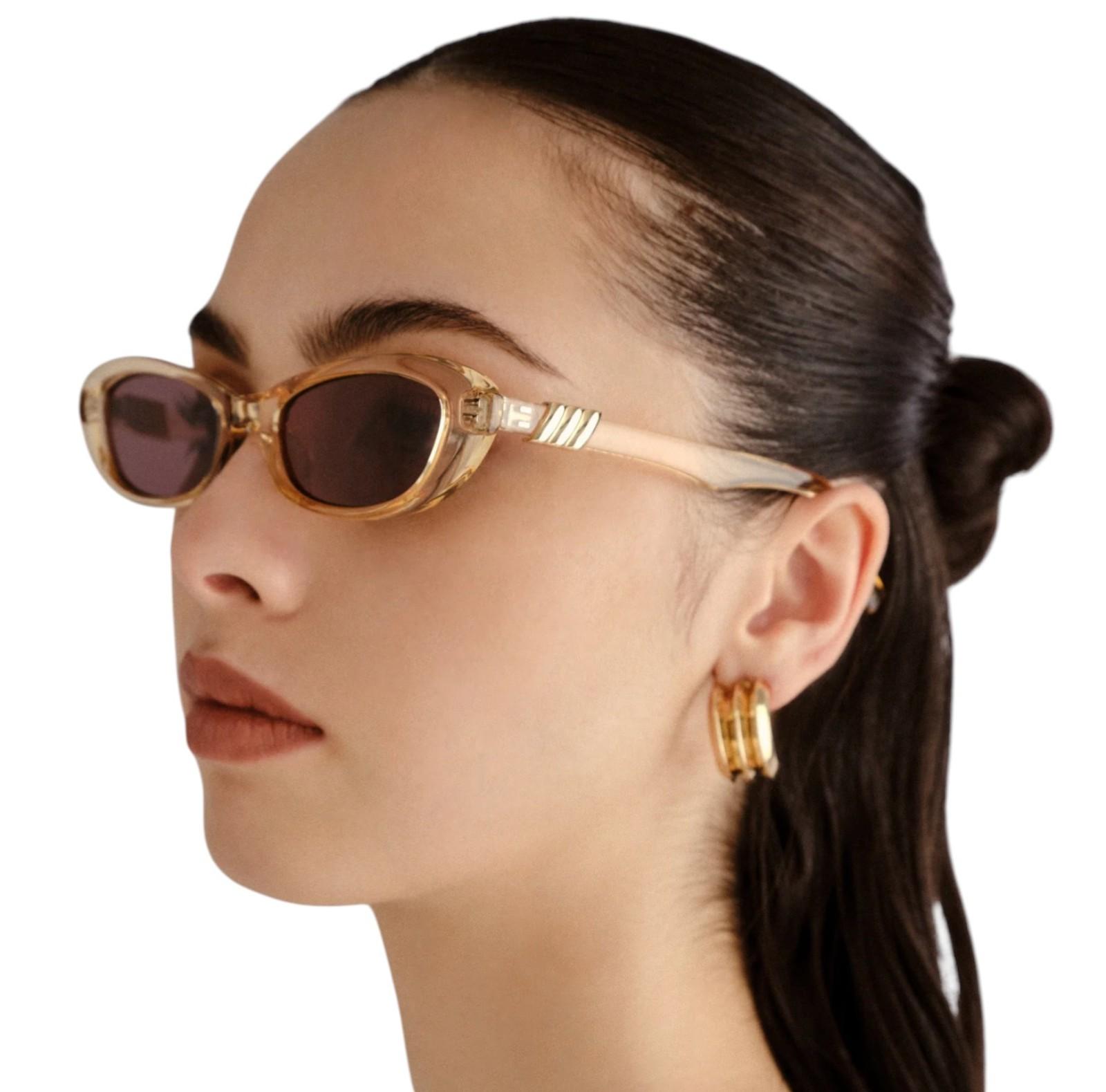 Woman wearing gold sunglasses and earrings on a white background