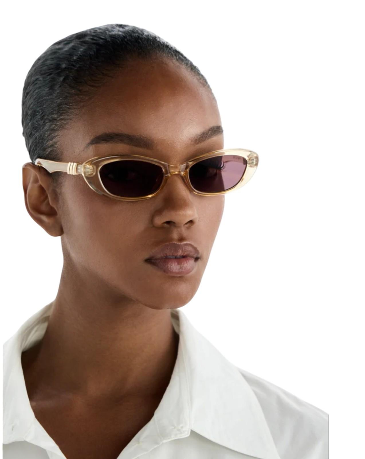 Woman wearing gold-framed sunglasses with a white shirt on a white background