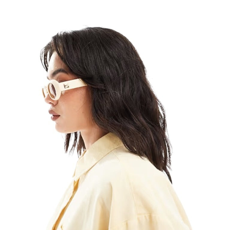 Woman wearing large round sunglasses and a light-colored shirt on a white background