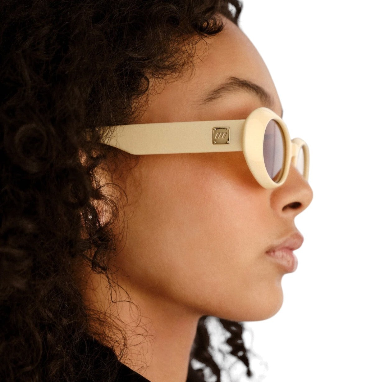 Close-up of a person wearing beige sunglasses with a brand logo.