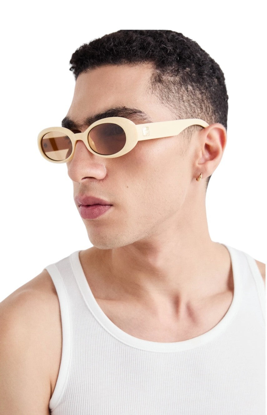 Person wearing beige sunglasses and a white tank top on a plain background