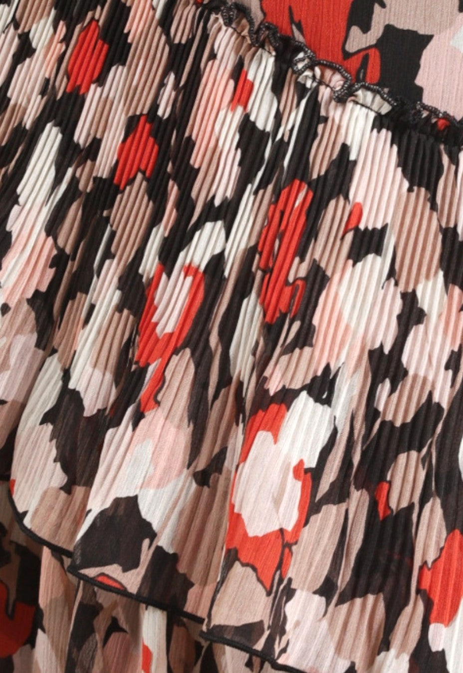 Close-up of a pleated fabric with a floral pattern featuring red, black, and beige colors.