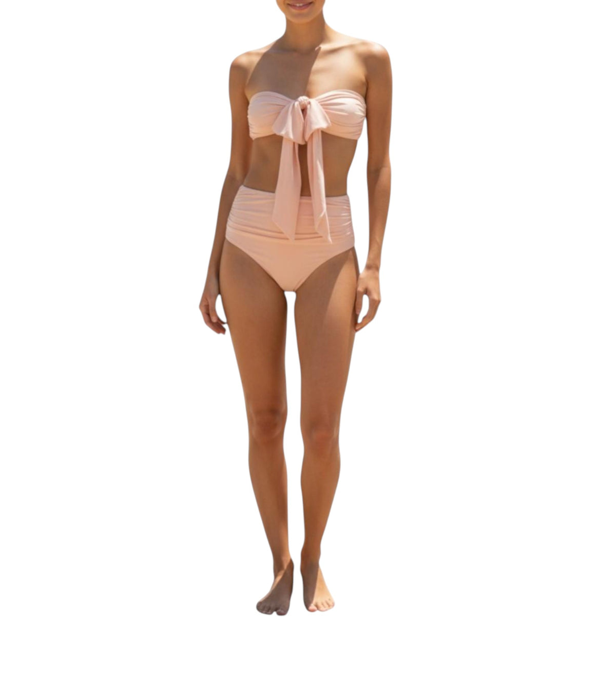 A woman modeling a two-piece bikini set in a pale peach-pink color. The top is a strapless bandeau style with a large front bow, and the bottoms are high-waisted with a ruched waistband.