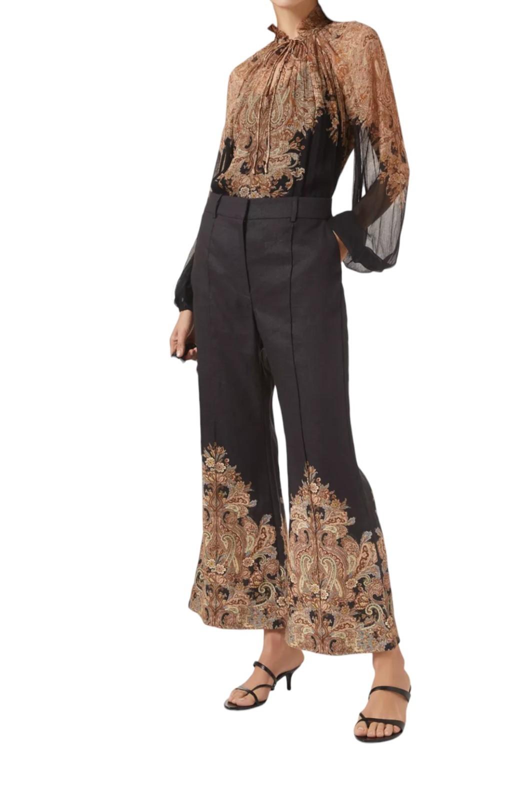 Woman wearing a patterned blouse and black pants with floral designs on a white background