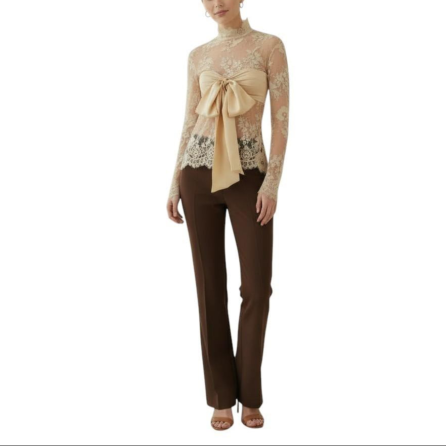 Woman wearing a beige lace top with a bow and brown pants on a white background