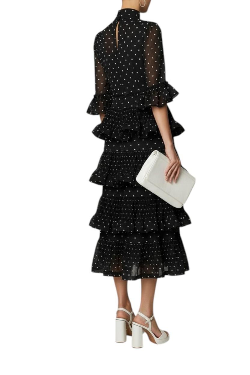 Woman wearing a black polka dot dress with ruffled layers on a white background