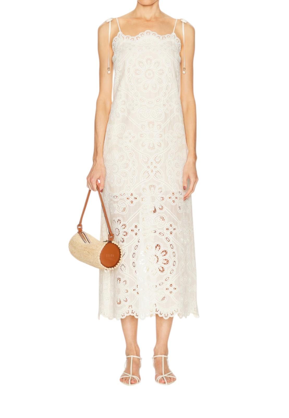 Woman wearing a white lace dress holding a round straw bag on a white background